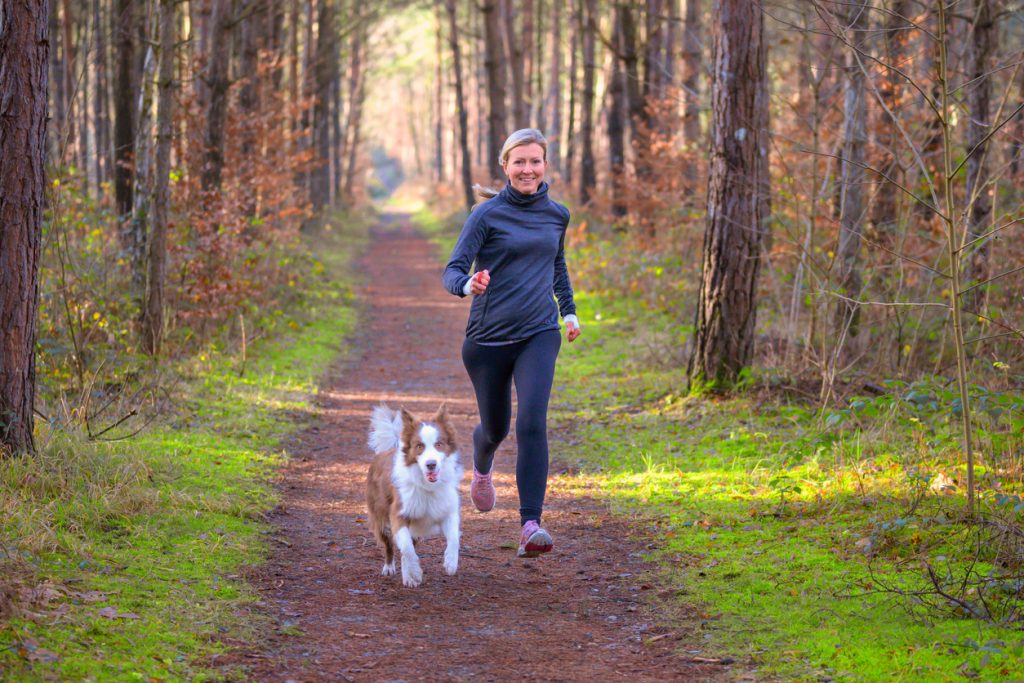 dog and owner jogging on a footpath in the woods
